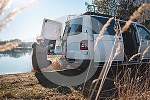 Young man with a converted van at a lake in nature