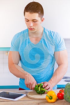 Young man cooking healthy meal vegetables tablet internet portrait format eating