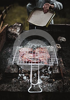 Young man cooking meat in the forest- Chef putting some meat skewers on grill in park outdoor - Summer, food concept - Focus on