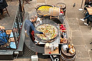 Young man cooking Paella in the outdoor bar of Covent Garden Apple Market in London.