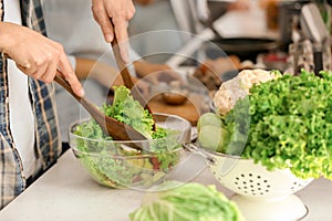 Young man cooking vegetable salad in kitchen