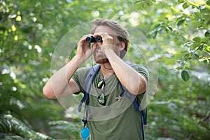 young man in countryside looking through binoculars