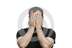 The young man covered his face with his hands. Brunette in a black T-shirt. Disturbing emotions. Isolated on white background