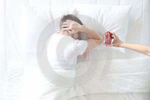 Young man covers his ears with his hands so as not to hear sound of alarm clock photo