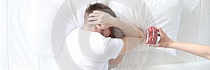 Young man covers his ears with his hands so as not to hear sound of alarm clock photo
