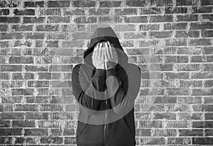 Young man covers his face with hands with bricks wall as background,black and white