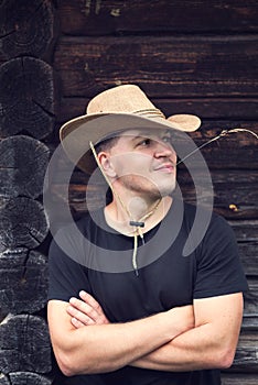 Young man in a cowboy hat on the background of a wooden log house