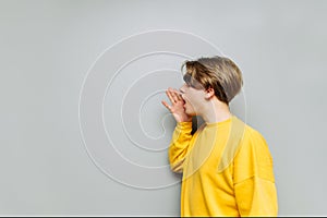 Young man cramps his palms to the side on copy space on a gray background. The guy speaks aside on an empty place on a background