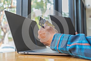 A young man with a credit card in his hand, sitting in agitation in front of a computer when he sees a debt collection document