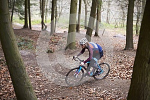 Young man cross-country cycling between trees in a forest