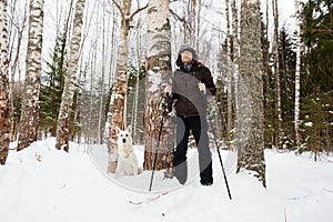 Young man cross-country skiing in the forest with White dog