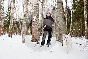 Young man cross-country skiing in the forest with White dog