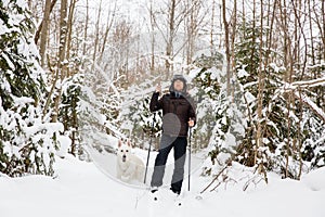 Young man cross-country skiing in the forest with White dog