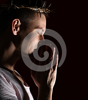 Young man in crown of thorns, martyr with closed eys imploringly clasped his hands side shot