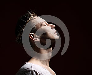 Young man in crown of thorns, martyr, saint holds his face lifted to sky. Side shot