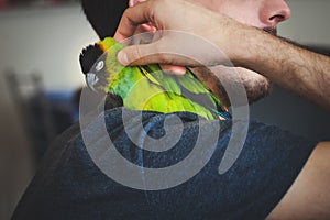 Young man cuddle his pet parrot on shoulder