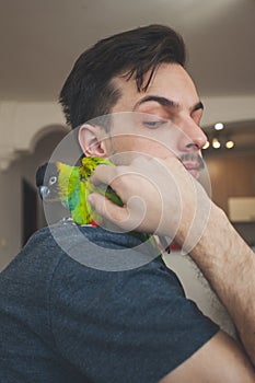 Young man cuddle his pet parrot on shoulder