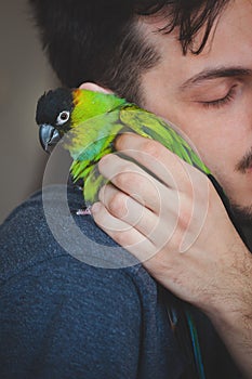Young man cuddle his pet parrot on shoulder