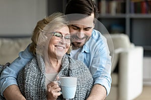 Young man cuddling wrapped in plaid smiling 60s elderly mother.