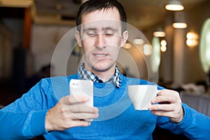 Young man with cup of coffee and smartphone