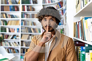 Young man with curly hair gesturing silence in a library setting