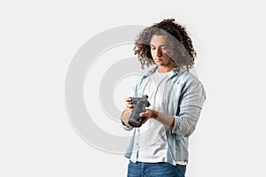 Young man with curly hair is holding a camera on his hand. Hobby and photography concept.