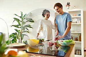 Young man cutting vegetables while woman watching him. Vegetarians preparing healthy meal in the kitchen together