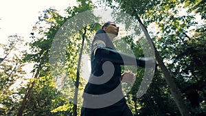 Young man cyborg jogs in the forest, wearing his special artificial hand. 4K.