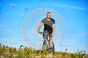 Young man cycling on a green meadow against blue sky with clouds.