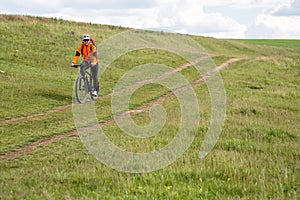 Young man cycling on a rural road through green meadow