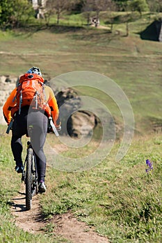 Young man cycling on a rural road through green meadow