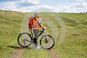 Young man cycling on a rural road through green meadow