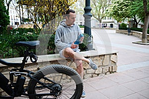 Young man cyclist drinking water from sports bottle in the city, relaxing after riding an eco-friendly electric bicycle