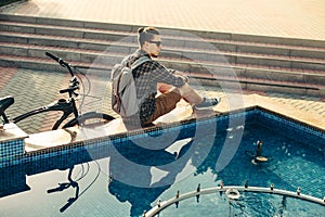 Young Man Cyclist Sitting Near Fountain Next To Bicycle In Summer Park Daily Lifestyle Urban Resting Concept