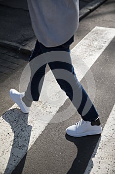 Young man in a dark trousers and sneakers crossing the road