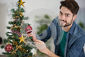 young man decorating artificial christmas tree