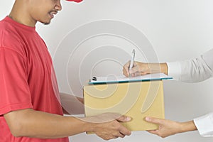 Young man delivering package to customer at home. Woman receiving a package from the courier and signing the form close-up