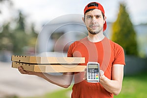 Young man is delivering pizza in boxes and holds payment terminal.