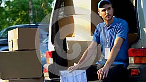 Young man from delivery service resting, sitting in van, loading of parcels