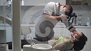 Young man dentist taking off his mouth, his work on the teeth of a patient in the dental office. Photographs the patient