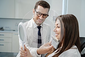 Young man dentist in white coat show veneers enamel color palette for beautiful patient woman