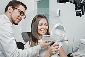 Young man dentist in white coat show veneers enamel color palette for beautiful patient woman