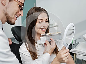 Young man dentist in white coat show veneers enamel color palette for beautiful patient woman