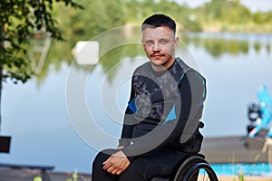 Young man with disability looking at camera sitting in wheelchair by lake