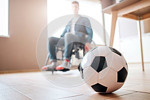 Young man with disability sitting on wheelchair and look down at ball for game. Ex sportsman. Upset and unhappy. Trauma