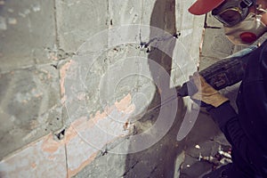 A young man dismantles an old tile from a concrete wall