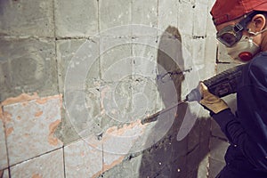 A young man dismantles an old tile from a concrete wall