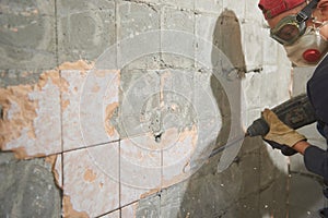 A young man dismantles old tile from a concrete wall