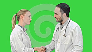 Young man doctor and beautiful nurse shaking hands after successful operation and looking at camera on a Green Screen