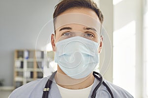 Young man doctor wearing medical mask with stethoscope looking at camera in clinic.